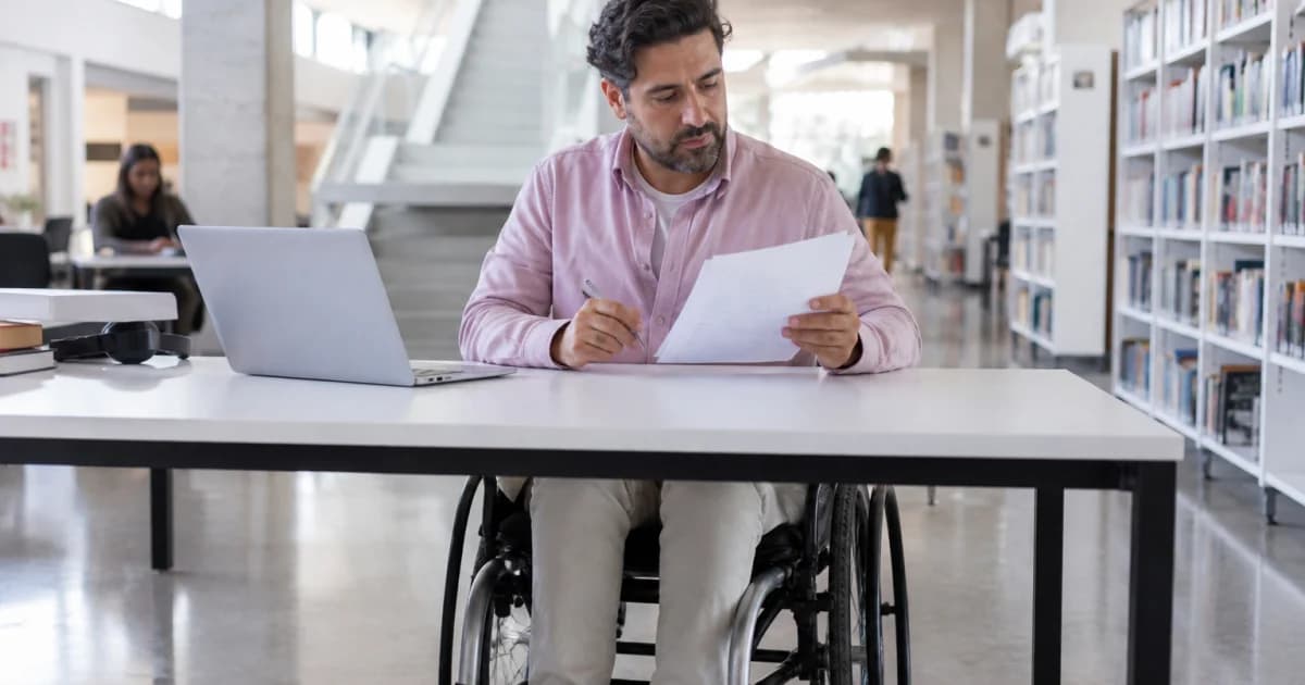 Profesional en silla de ruedas revisando una candidatura en una biblioteca accesible